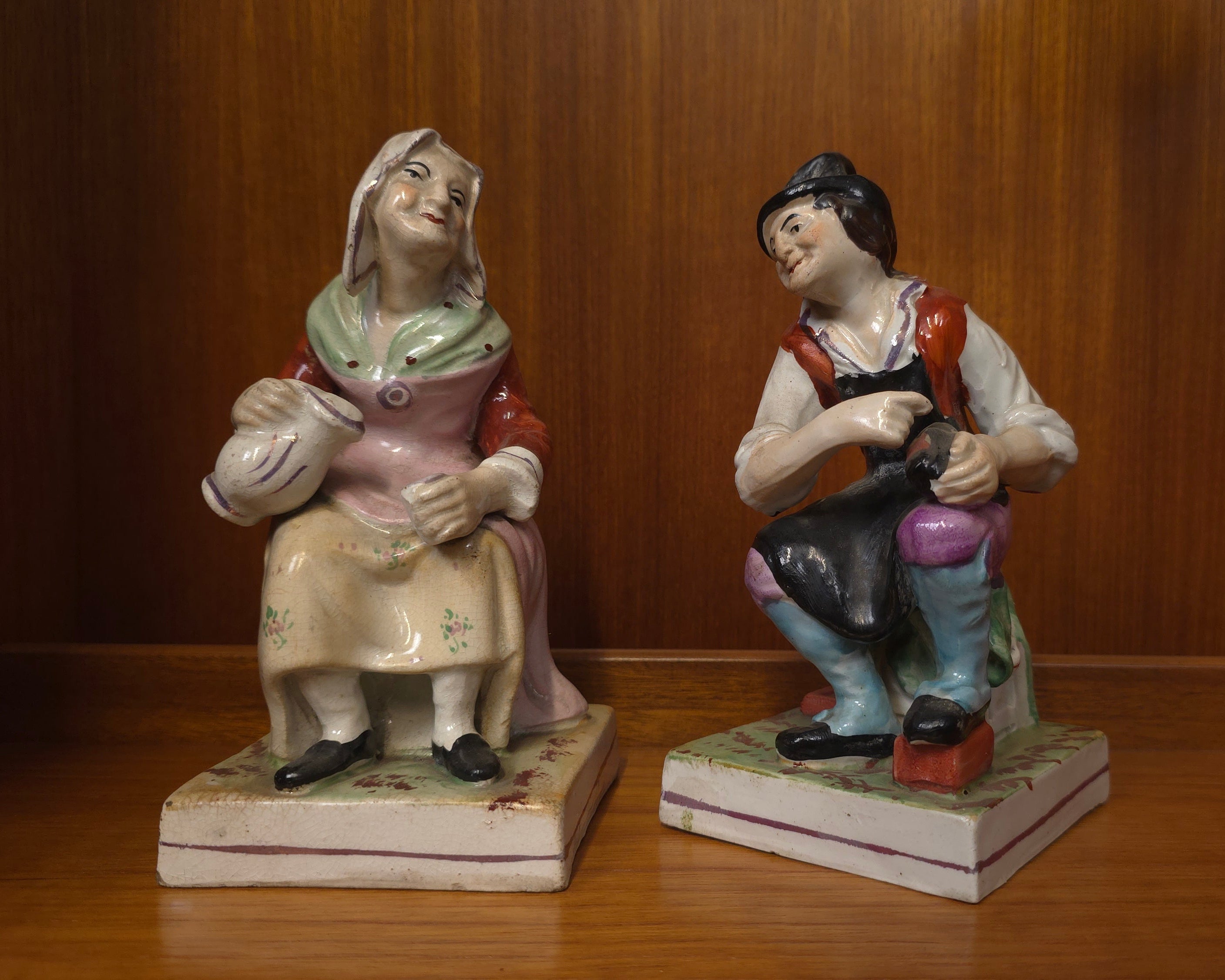 Two ceramic figurines of a man and a woman on a wooden surface with a wooden background